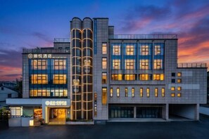 Un hotel moderno con una estructura cilíndrica destacada, múltiples ventanas y una fachada bien iluminada.