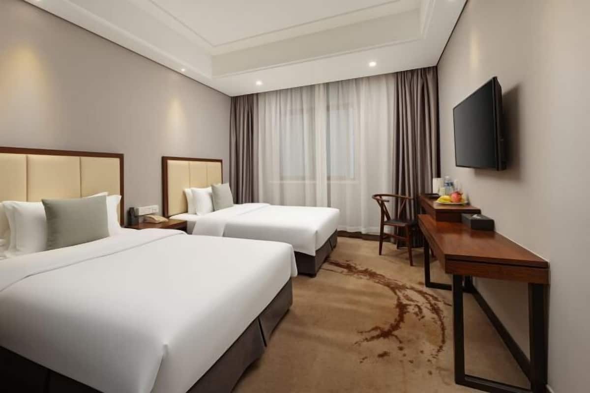 A hotel room with two beds, a desk, a chair, a TV, and a window with curtains.
