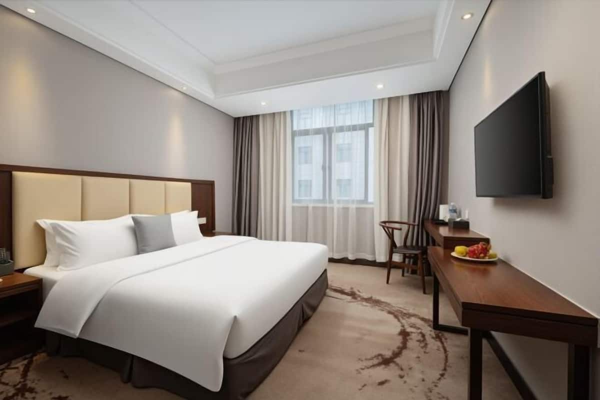 A hotel room with a bed, a desk, a chair, a TV, and a window with curtains.