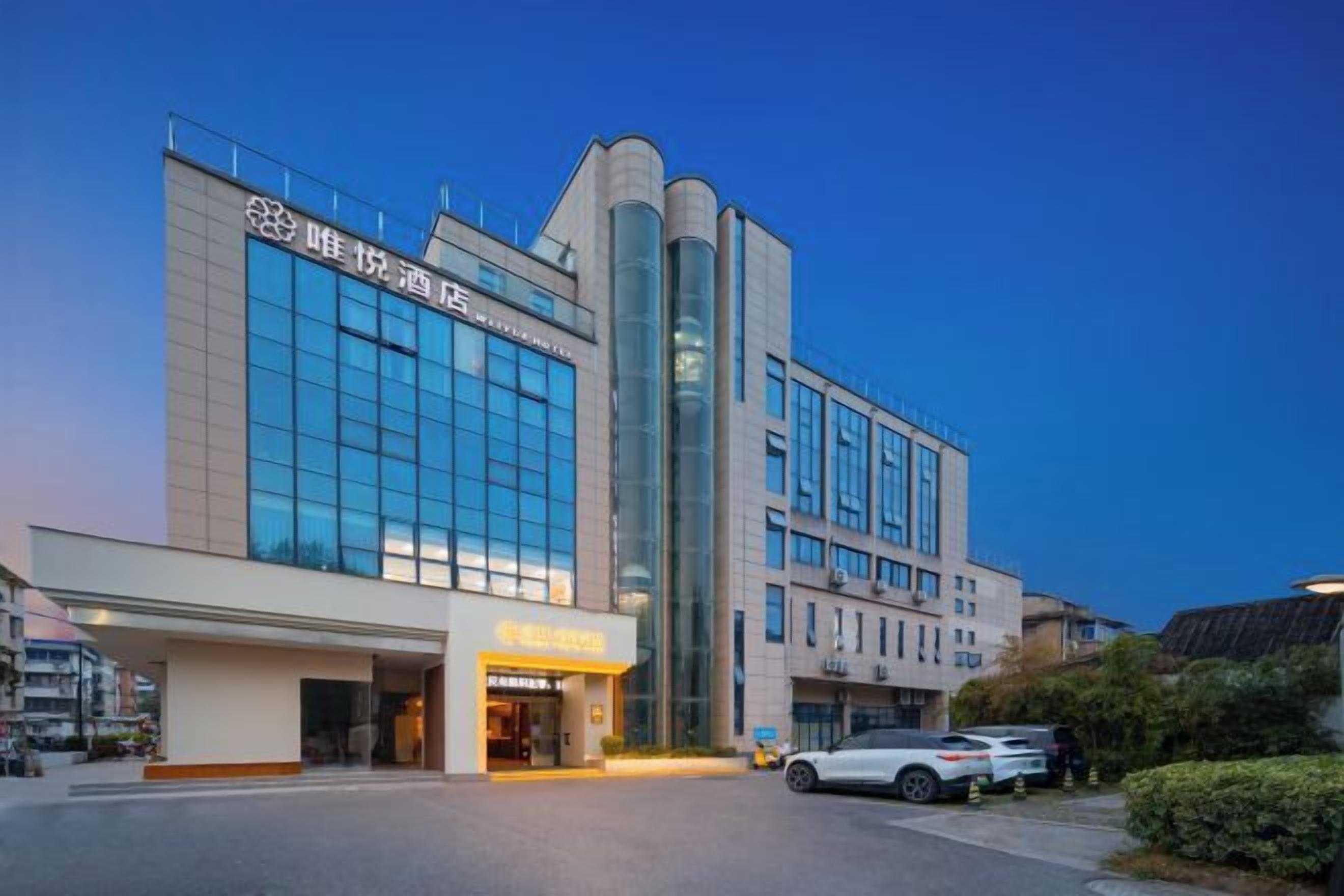 A modern hotel with a prominent entrance, large windows, and a parking area.