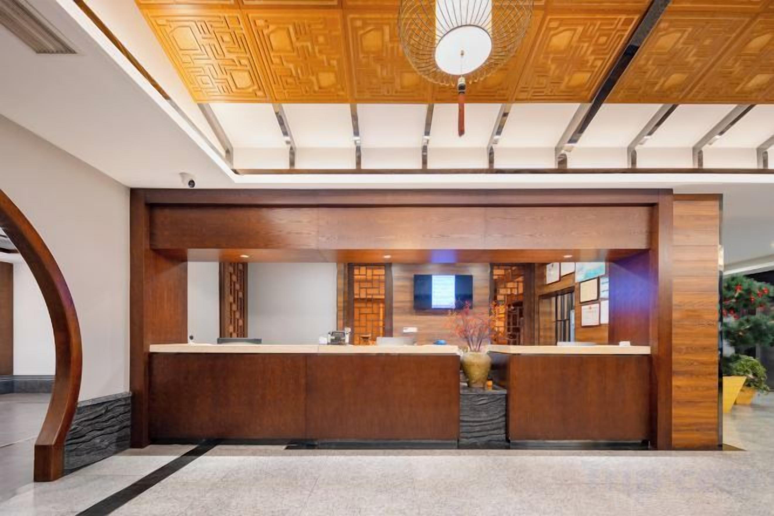 A reception area with a wooden reception desk, a flat-screen TV, and a ceiling with a geometric pattern.