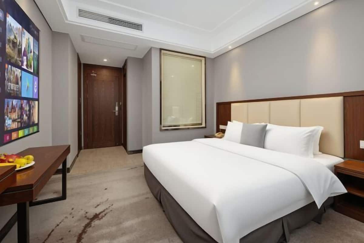 A hotel room with a large bed, a desk with a chair, a window, and a door.