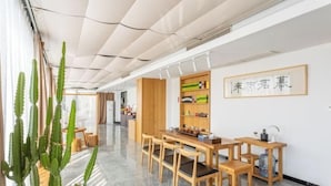 Een moderne eetruimte met een lange tafel en stoelen, een houten kast met planken en een grote cactus.
