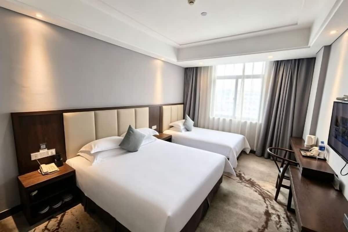 A hotel room with two beds, a desk, a TV, and a window with curtains.