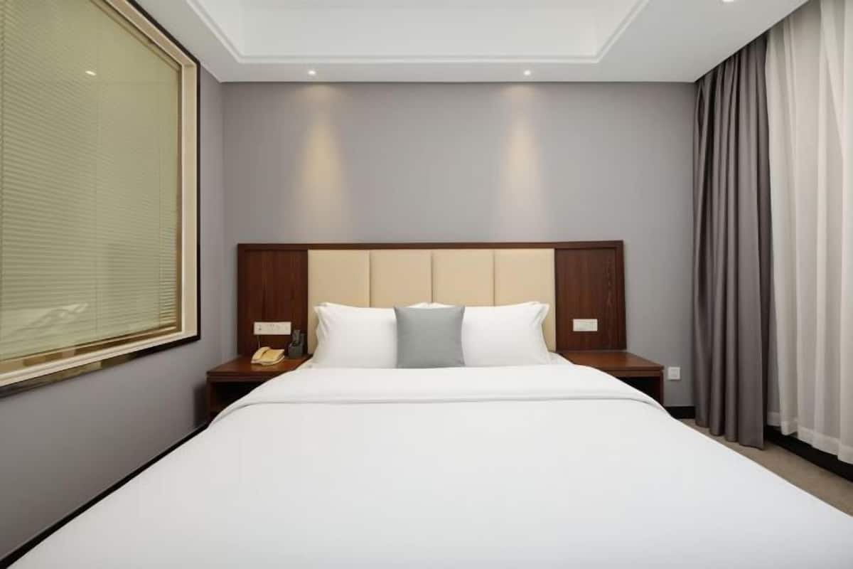 A hotel room with a large bed, a wooden headboard, two bedside tables, and a window with blinds.