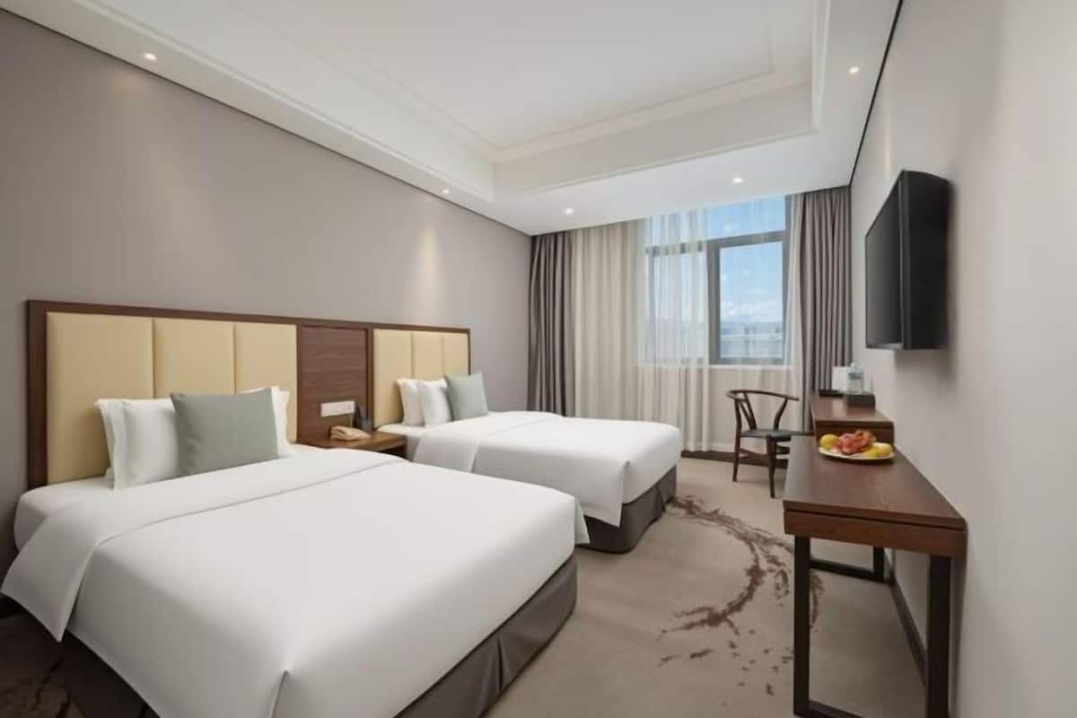 A hotel room with two beds, a desk, a chair, and a TV.