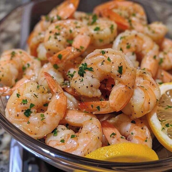 A plate of cooked shrimp garnished with herbs and lemon slices.