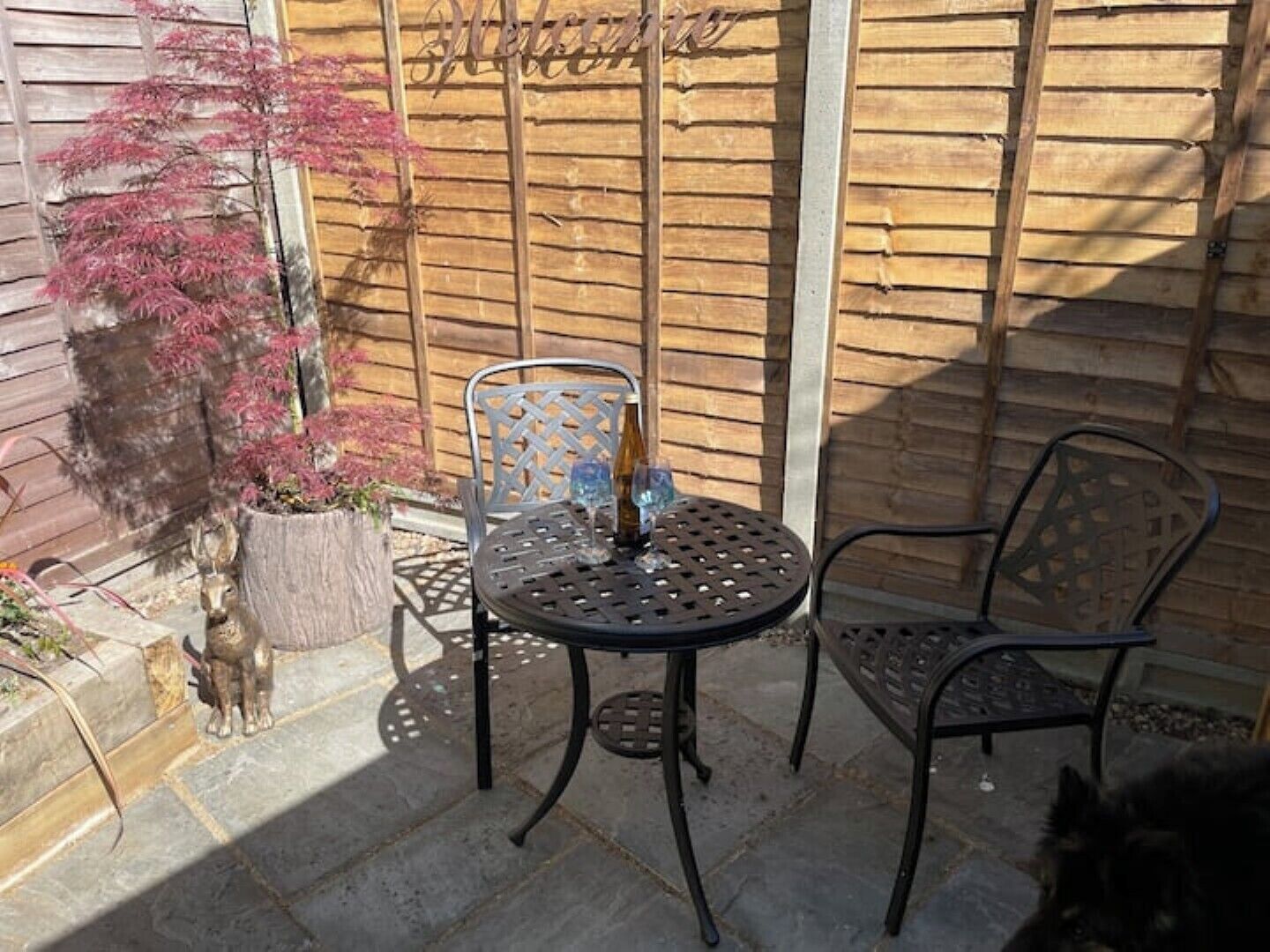 An outdoor patio with a round table and two chairs, a potted plant, and a decorative metal sign.