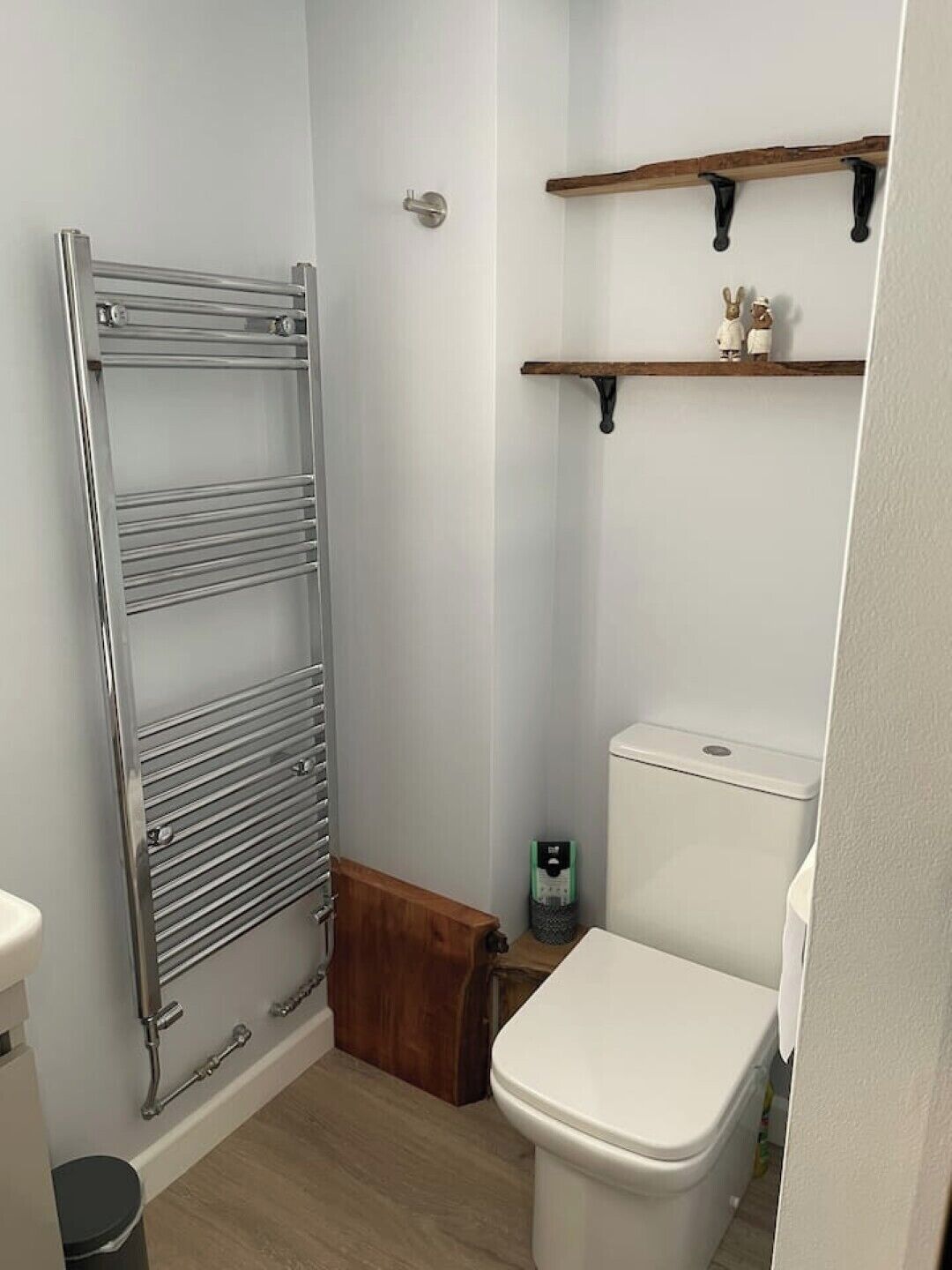 A small bathroom with a toilet, a metal towel rack, and two wooden shelves above the toilet.