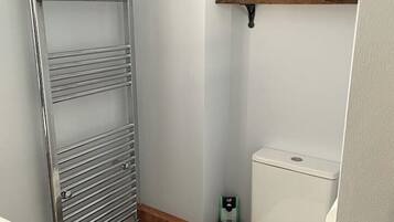 A small bathroom with a toilet, a metal towel rack, and two wooden shelves above the toilet.