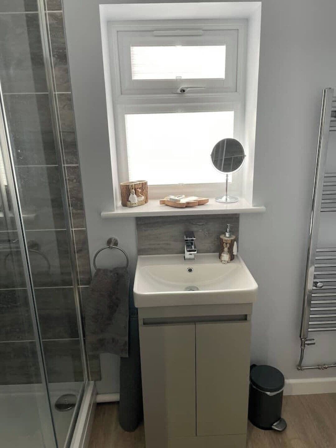 Een badkamer met een douchecabine van glas, een witte wastafel met een spiegel erboven en een handdoekrek.