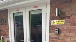 Una puerta de marco blanco con un panel de vidrio, un letrero de precaución y un timbre.