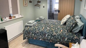 Un dormitorio con cama, un radiador, una ventana con persianas, una puerta y un estante con objetos.