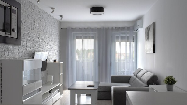 A modern living room with a grey sofa, a white coffee table, and a TV on a white cabinet. - RentPlanet - Apartament przy Lotnisku (Poznań)