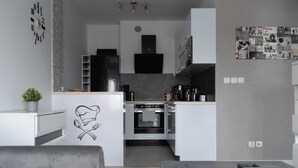 A modern kitchen with a central island, built-in oven, and a flat-screen TV mounted above the oven. - RentPlanet - Apartament przy Lotnisku (Poznań)