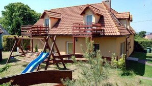 Ein zweistöckiges Haus mit rotem Ziegeldach, einer Holzterrasse und einer Schaukel.
