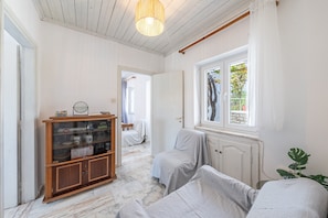 Un couloir avec une armoire en bois, deux fauteuils recouverts de tissu, une fenêtre donnant sur un paysage agréable et un luminaire suspendu.