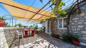 A stone building with a patio, outdoor seating, and potted plants. - Apartment 'Ambelaki' with Sea View, Private Garden and Wi-Fi (Antípaxos)