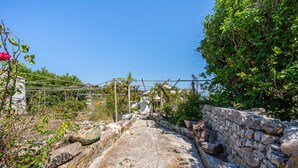 A stone pathway leading to a building, surrounded by greenery and a pergola with climbing plants. - Apartment 'Ambelaki' with Sea View, Private Garden and Wi-Fi (Antípaxos)