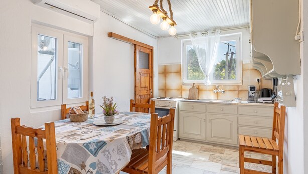 A kitchen with a stove, sink, and cabinets, a dining table with chairs, and a ceiling fan. - Apartment 'Ambelaki' with Sea View, Private Garden and Wi-Fi (Antípaxos)
