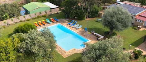 A swimming pool with multiple sun loungers and a small garden area.