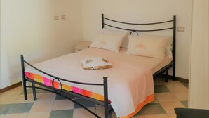 A single bed with a metal frame, a white mattress, and a pink bedspread in a room with a checkered floor and white walls. - Studio 'Ulivo' with Shared Pool, Wi-Fi and Air Conditioning (Alghero)
