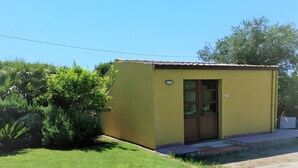 A small yellow building with a door and windows, surrounded by a well-maintained lawn and greenery. - Studio 'Ulivo' with Shared Pool, Wi-Fi and Air Conditioning (Alghero)