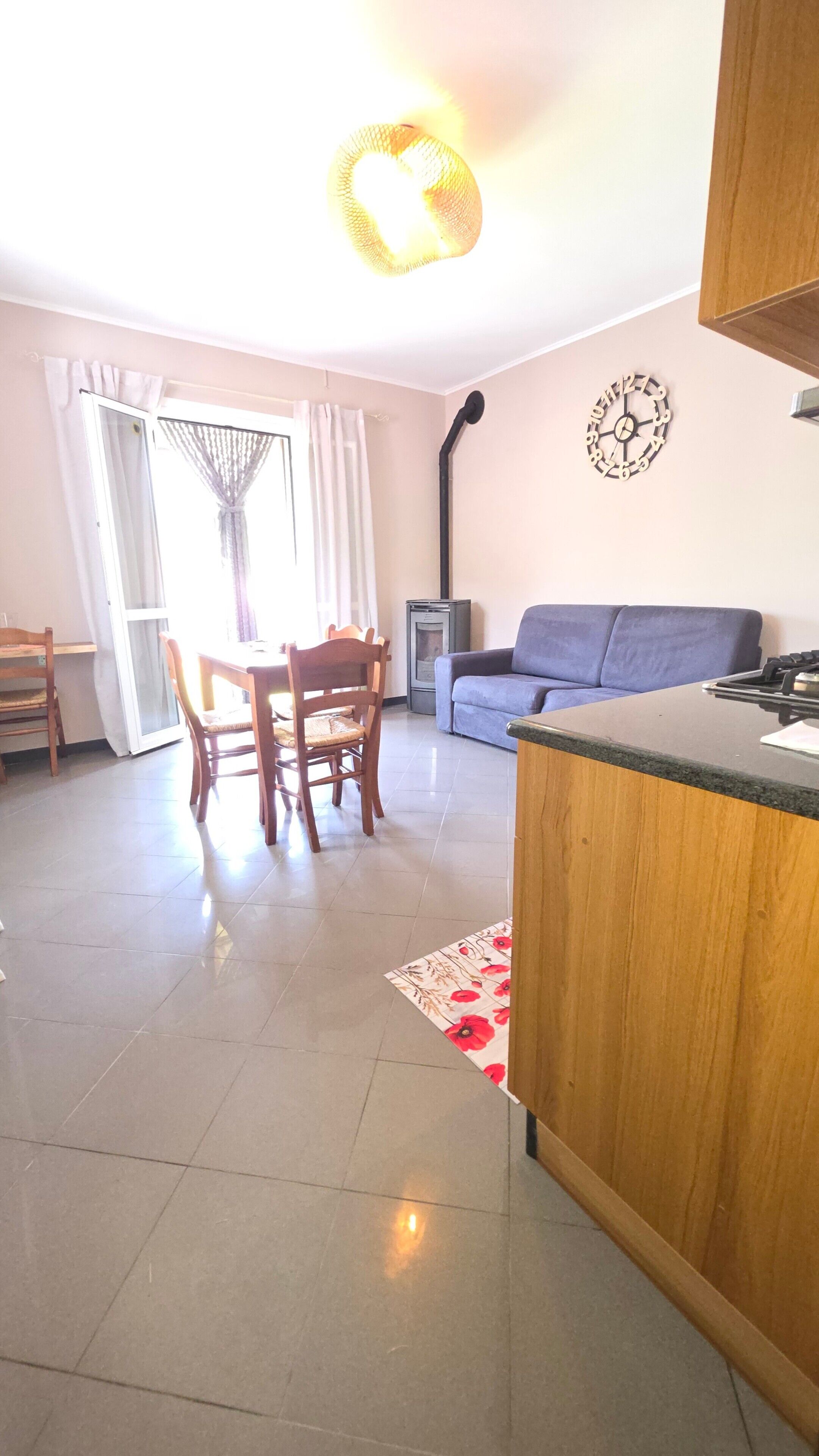 Un salon avec un canapé, une table à manger avec des chaises, un coin cuisine avec une cuisinière et une horloge au mur.