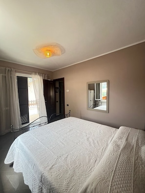 Un dormitorio con cama, ventilador de techo, ventana con cortinas y espejo en la pared.