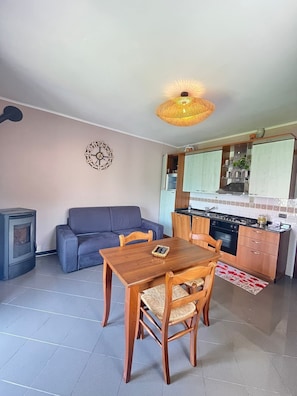 Un espacio habitable compacto con una mesa de comedor, sofá, kitchenette y un reloj de pared decorativo.