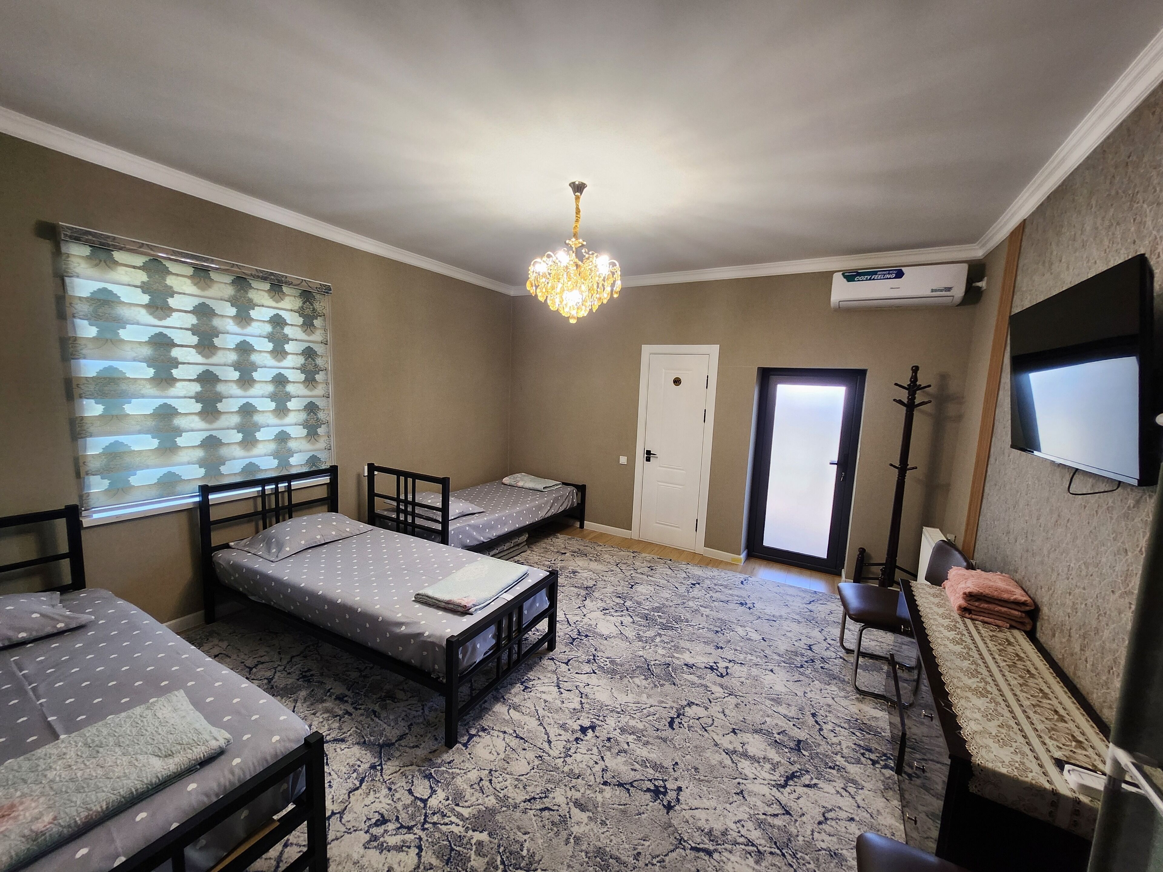 Une petite chambre meublée, comprenant deux lits simples, un bureau, une chaise, une télévision et un lustre.