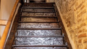A wooden staircase with a handrail, leading upwards in a stone-walled corridor.