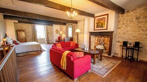 A spacious living room with a red sofa, wooden flooring, a chandelier, a fireplace, and a stone wall.