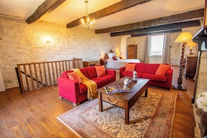 A room with a wooden floor, a red sofa set, a wooden coffee table, a patterned rug, and a stone wall. - The Logis de la Bastide (Lauzerte)