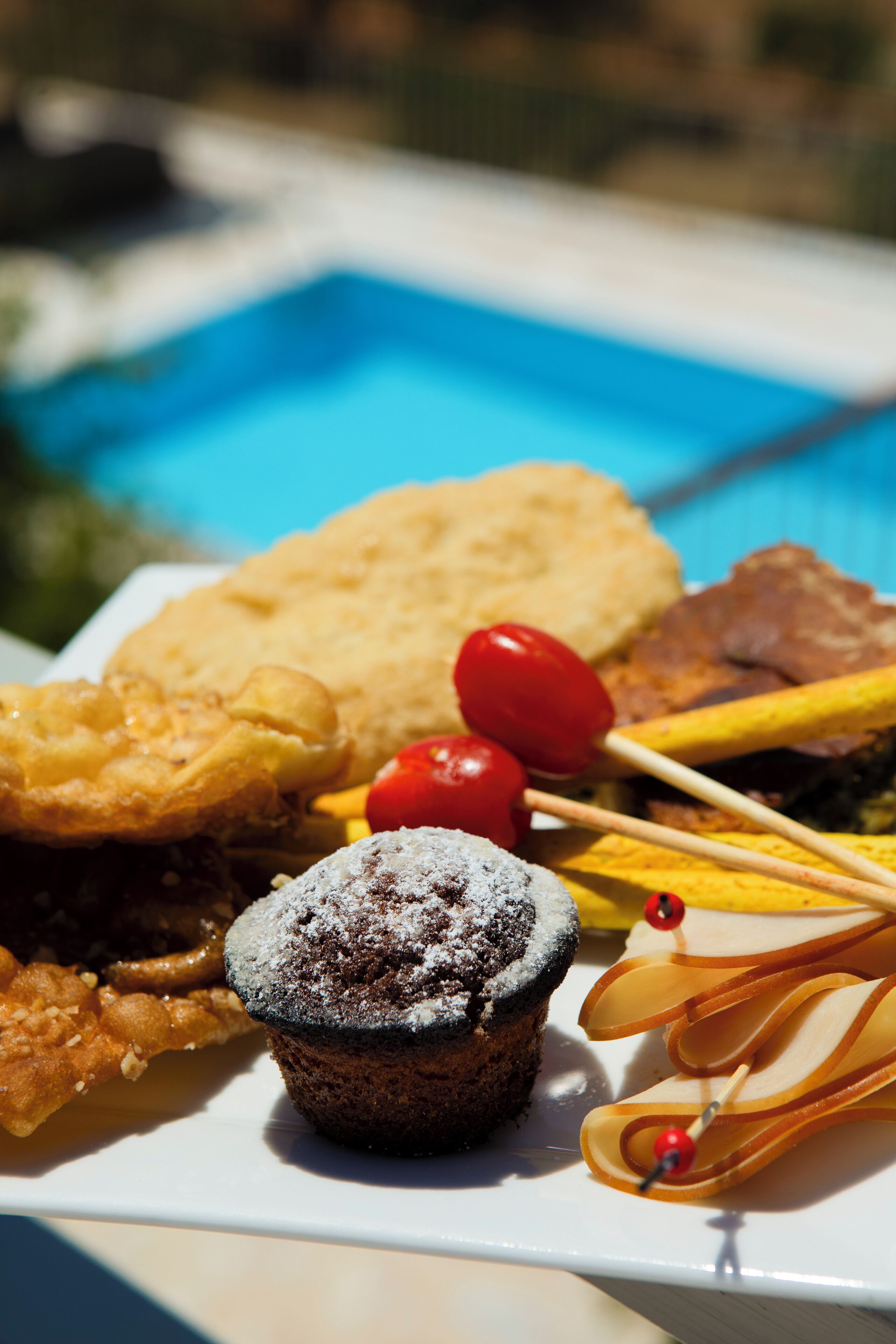 A plate of assorted desserts including a muffin, fritters, and fruit skewers.