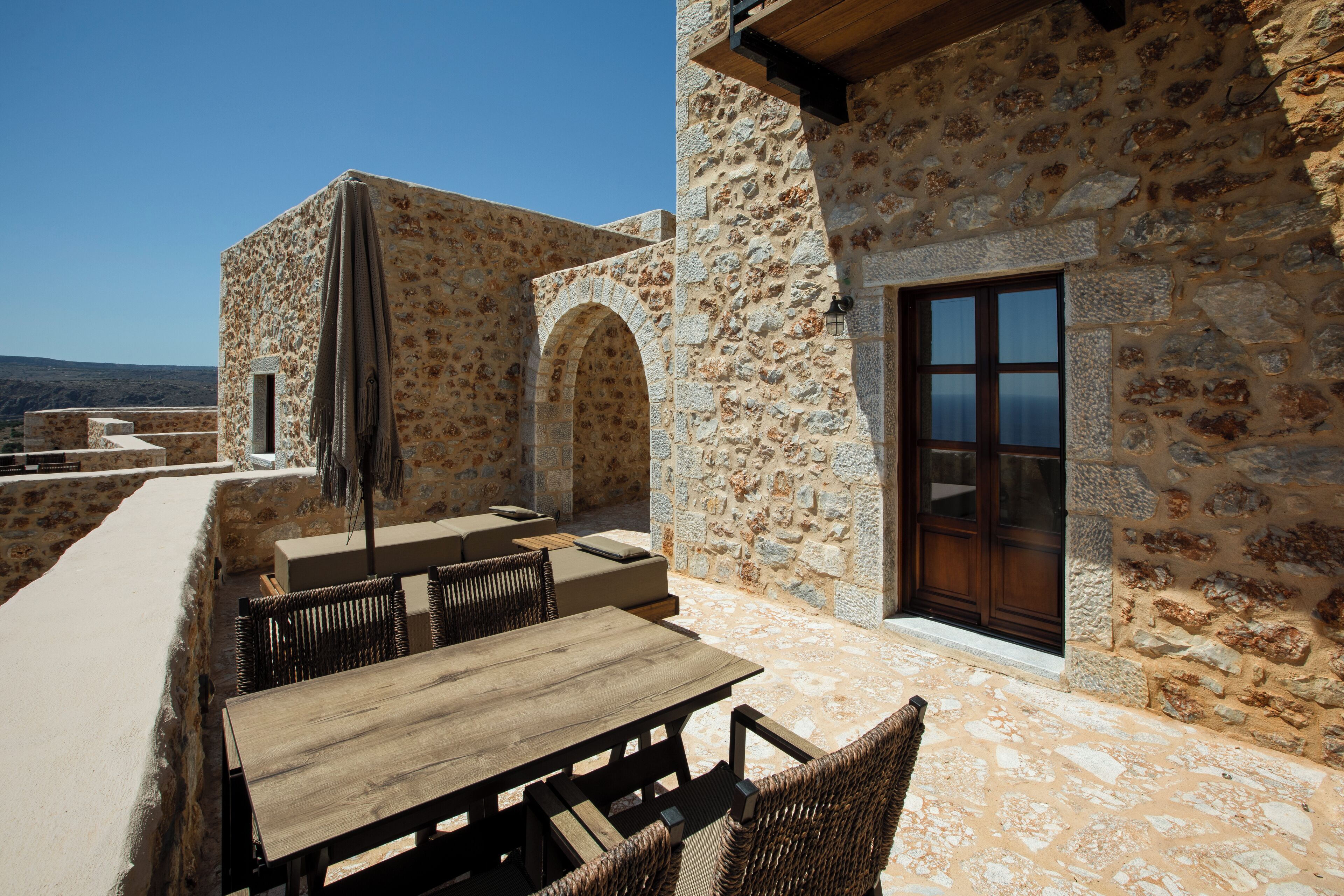 Une terrasse extérieure avec des murs en pierre, une table en bois et des chaises en osier.