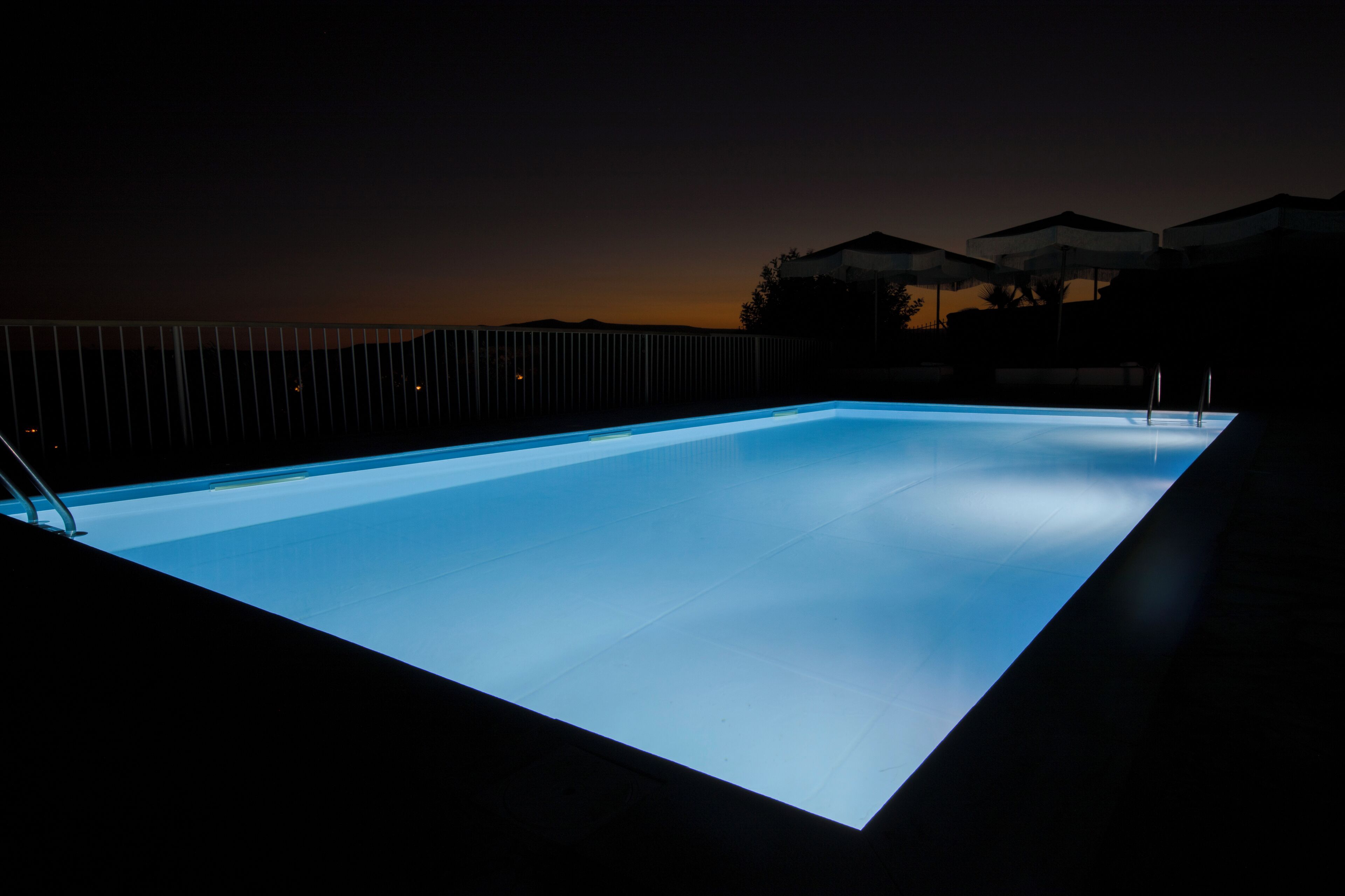A rectangular swimming pool with a dark surrounding area and a fence.