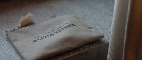 A small, beige fabric pouch with the text "OLIVIA THINKS" and "ESTD 1870" on a textured surface.