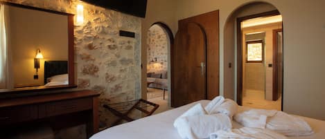 Habitación de hotel con pared de piedra, cómoda de madera, cama con ropa blanca y televisor de pantalla plana sobre la cómoda.