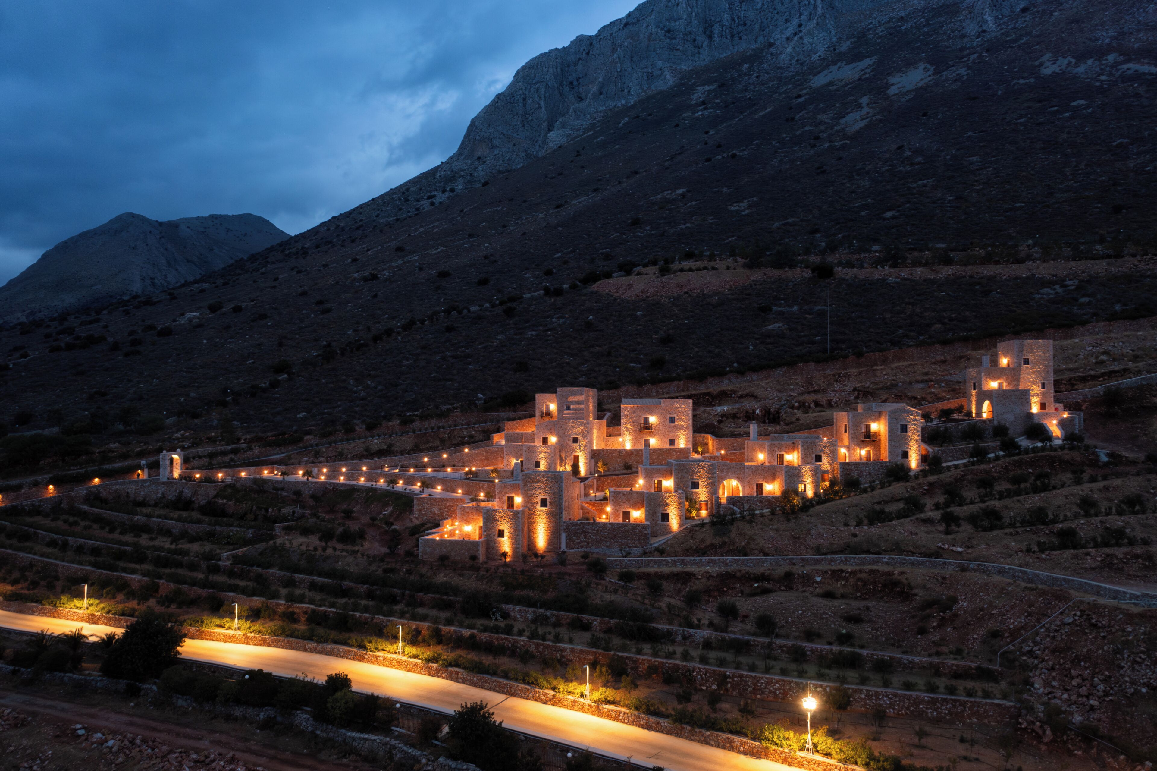 A terraced village with stone buildings, a winding road, and a mountain in the background.