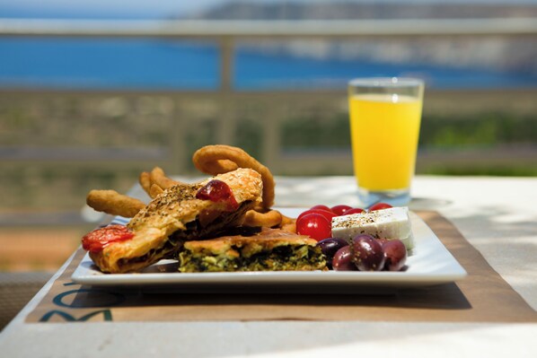 A plate of food with a glass of orange juice on a table with a view. - Anemos Suites Mani (East Mani)