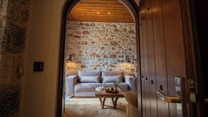 An interior with a stone wall, wooden ceiling, a sofa, a coffee table, and a door. - Anemos Suites Mani (East Mani)