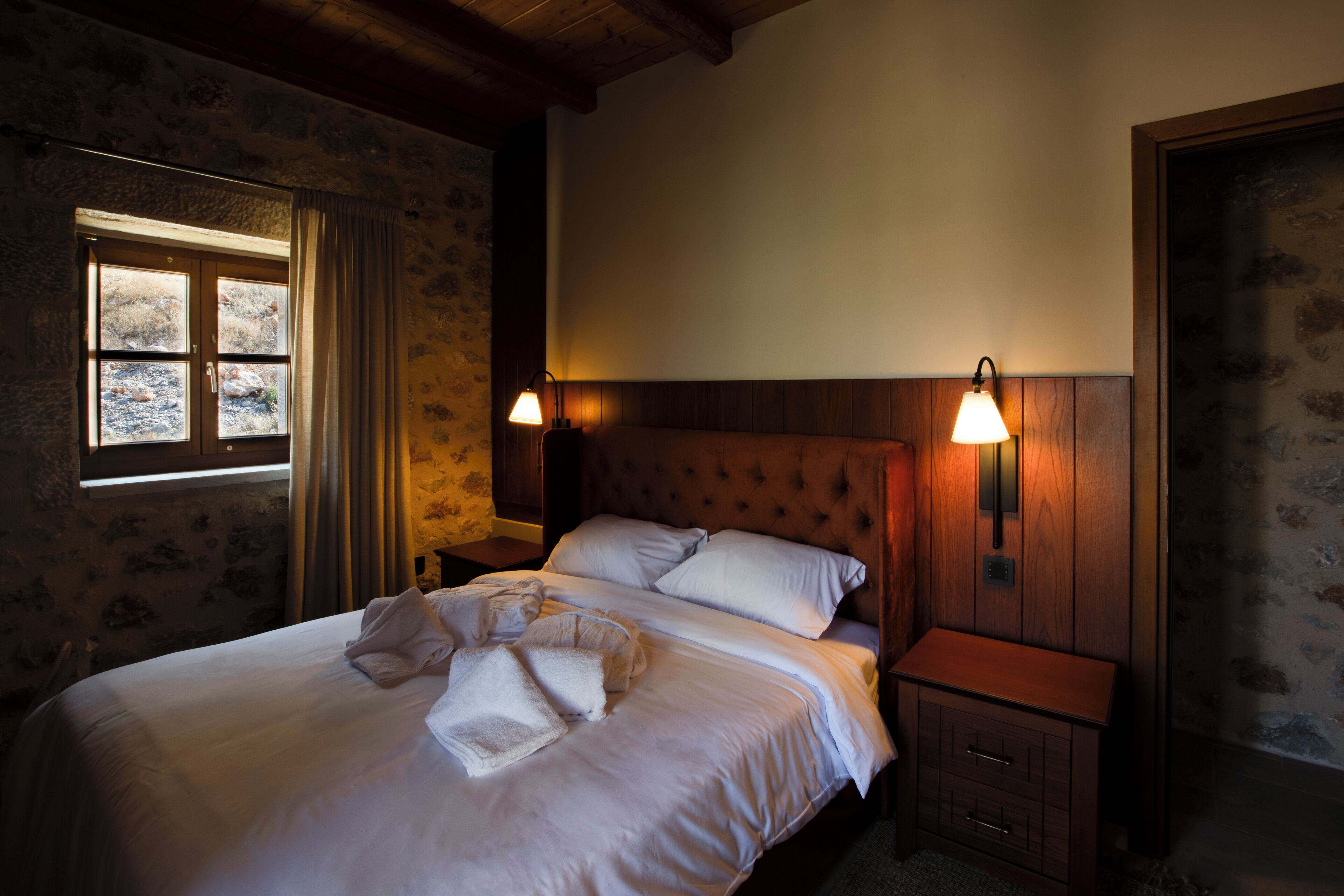 Ein ordentlich bezogenes Bett mit Kissen und Decke, zwei Nachttische mit Lampen und ein Fenster mit Vorhängen.