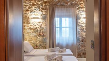 A bedroom with a stone wall, a wooden ceiling, a bed with white linens, and a window with curtains.