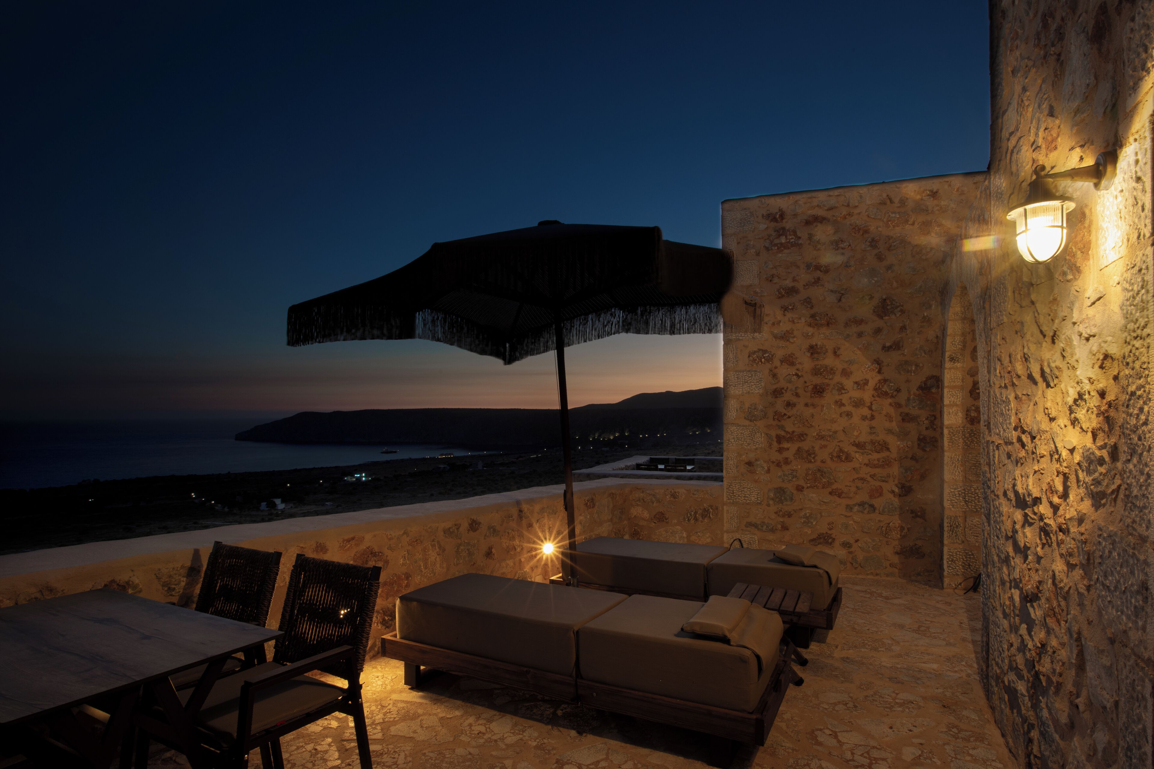 A terrace with stone walls, a table, two lounge chairs, and an umbrella.