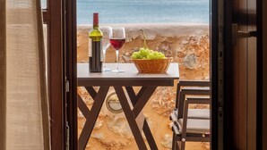 A balcony with a table set for two, a bottle of wine, a glass, and a basket of grapes. - Anemos Suites Mani (East Mani)