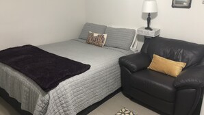 A bedroom with a bed, a black leather chair, a bedside table with a lamp, and a small framed picture on the wall. - Cozy, centralized Studio in wonderful Houston with WiFi, AC (Houston)