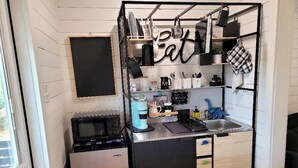 A compact kitchen with a microwave, coffee maker, and a sink. There is a chalkboard on the wall and a shelf with kitchen utensils. - Dinosaur Crossing Guesthouse With Loft (Glen Rose)