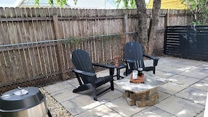 A patio area with two Adirondack chairs, a small stone table, and a portable grill. - Dinosaur Crossing Guesthouse With Loft (Glen Rose)