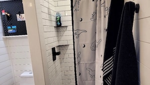 A shower area with a glass door, a white toilet, and a wooden floor. - Dinosaur Crossing Guesthouse With Loft (Glen Rose)